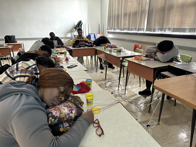 Students resting their heads on desks in a classroom setting, appearing to be taking a break or participating in a relaxation activity. Des étudiants posent leur tête sur des bureaux dans une salle de classe. Ils semblent faire une pause ou participer à une activité de relaxation.